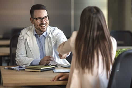 doctor shaking hands with patient over desk